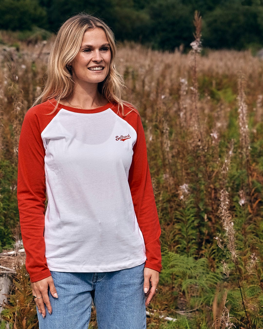 A woman standing in a field wearing a Saltrock Carolina Womens Long Sleeve Raglan T-Shirt - Red/White.