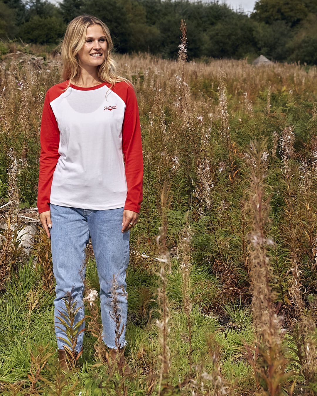 A woman standing in a field wearing a Saltrock Carolina - Womens Long Sleeve Raglan T-Shirt - Red/White.