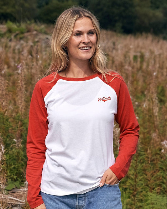 A woman is standing in a field wearing a Saltrock Carolina - Womens Long Sleeve Raglan T-Shirt - Red/White.