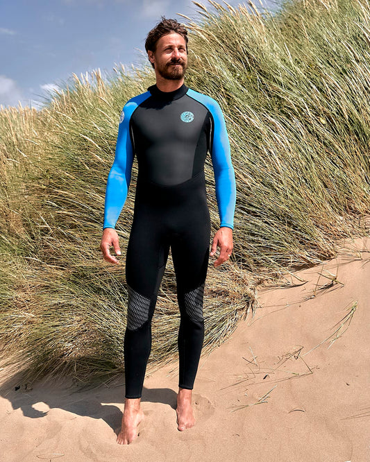 A man in a Saltrock Core - Mens 3/2 Full Wetsuit - Blue/Black standing in a sand dune.