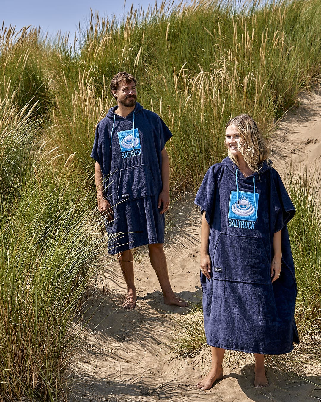 A man and a woman dressed in Saltrock ponchos on a beach.