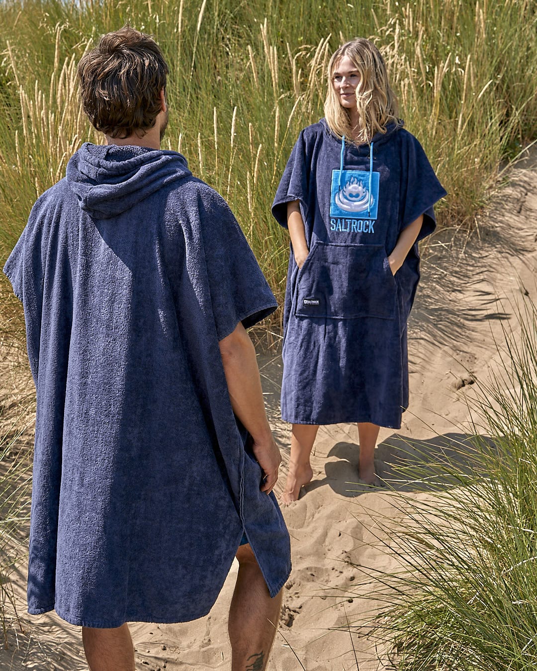 A man and woman standing on a beach in a Saltrock Corp - Changing Towel - Blue.