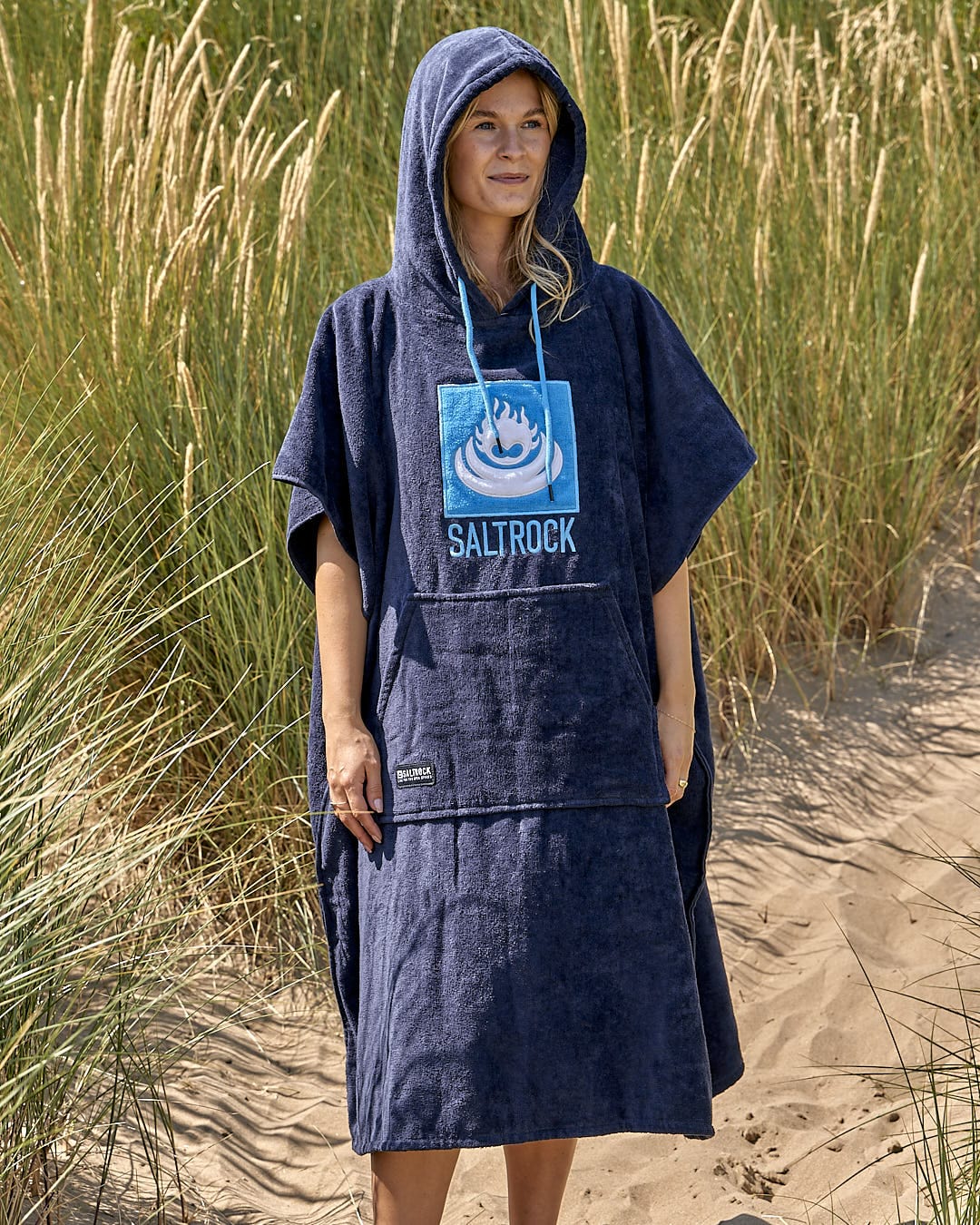 A woman wearing a Saltrock hooded poncho on the beach.
