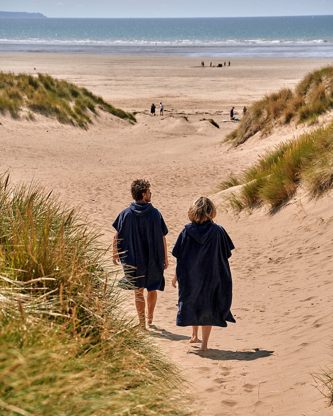 Two people walking down a path on a beach with the Corp - Changing Towel - Blue from Saltrock.