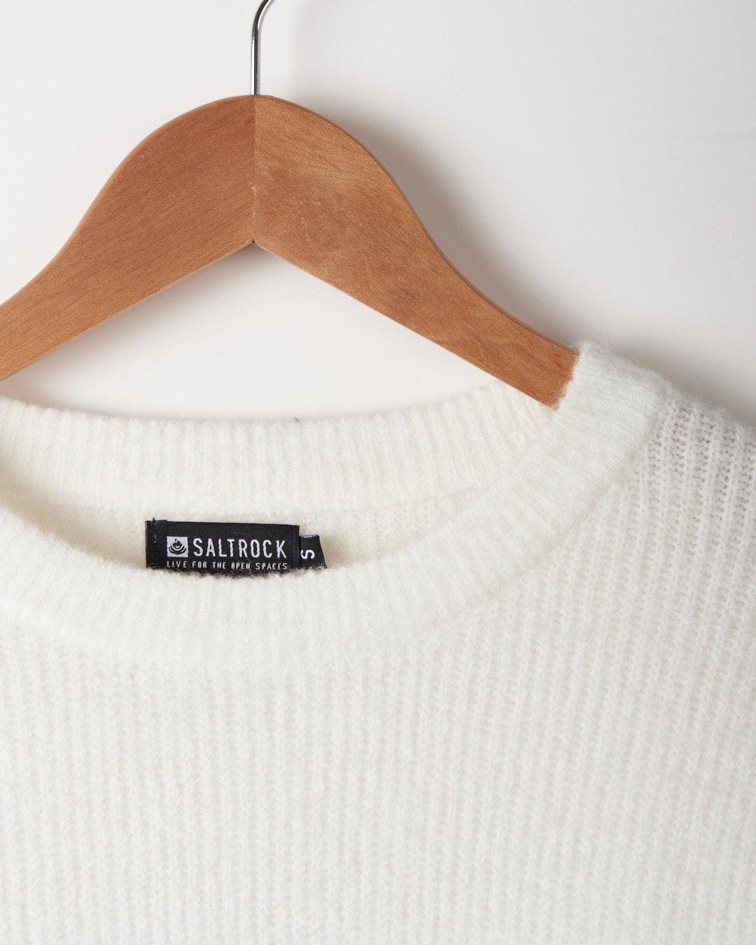 A Darcy - Womens Knitwear - White sweater hangs on a wooden hanger, showcasing its soft touch. (Saltrock)