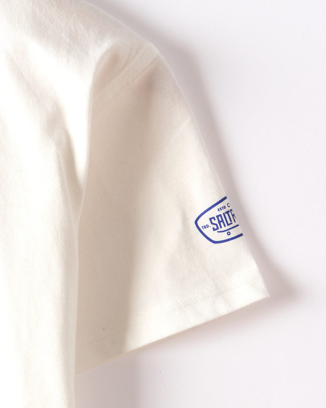 Close-up of the Saltrock Dawn Ready Kids T-Shirt in white, made from 100% cotton, featuring a small blue "SHOT" logo patch on the sleeve near the hem.
