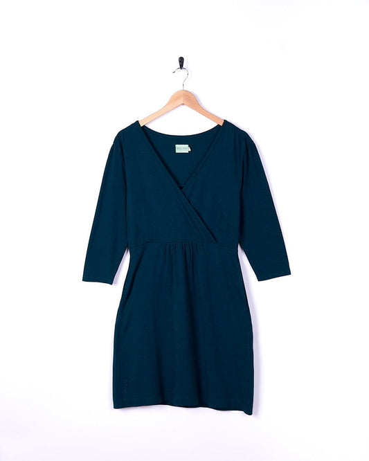 A Della - Womens Wrap Top Dress in a dark blue color, hanging on a hanger with the brand name Saltrock.
