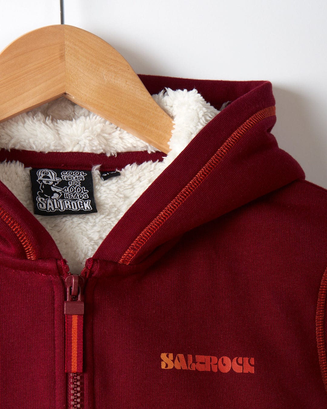Red kids' Sherpa lined hoodie on a wooden hanger, displaying distinctive "Saltrock" branding in orange on the front and an inside label.