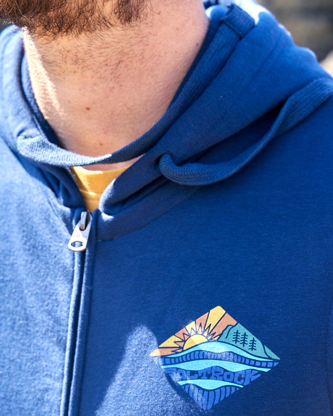 A man wearing a Saltrock Diamond Scene - Mens Zip Hoodie - Blue with a blue and yellow logo.