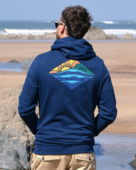 A man is standing on the beach wearing a Saltrock Diamond Scene - Mens Zip Hoodie - Blue.