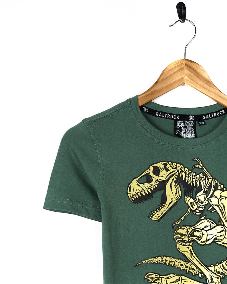 A cool and stylish Saltrock Dinosk8 - Kids Short Sleeve T-Shirt - Green featuring a dinosaur riding a skateboard.