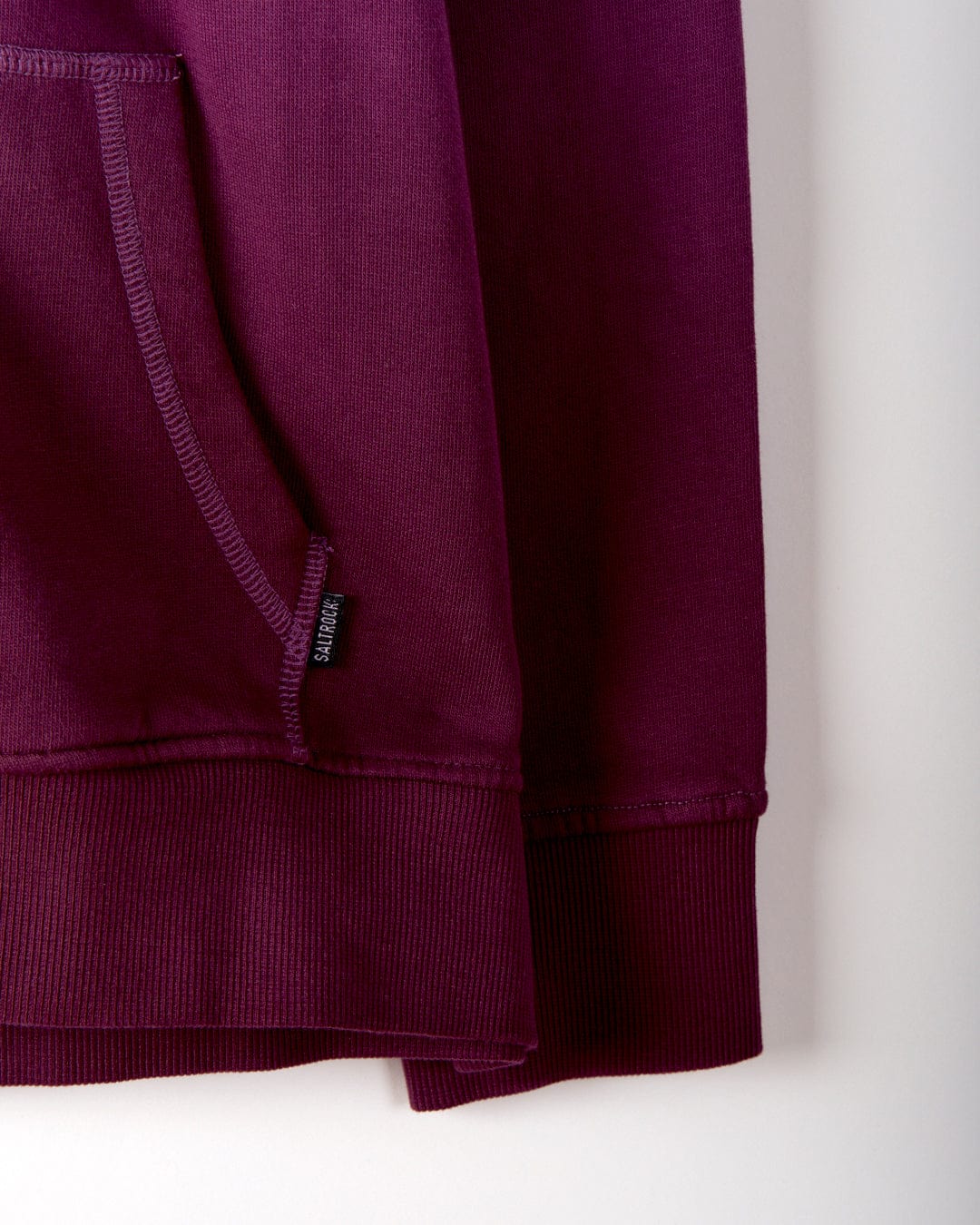 A close-up of the Dip Dye Women's Zip Hoodie in a maroon shade reveals a dip dye print, complete with a visible pocket and a small black tag on the seam. Made from 100% cotton, this Saltrock hoodie boasts subtle branding that enhances its casual allure.