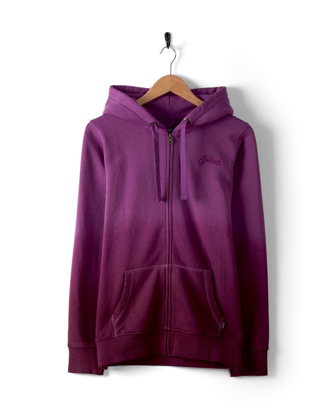A Dip Dye - Womens Zip Hoodie in purple, showcasing the Saltrock brand, crafted from 100% cotton, hangs on a wooden hanger. The front zipper and pockets enhance its functionality against the crisp white background.