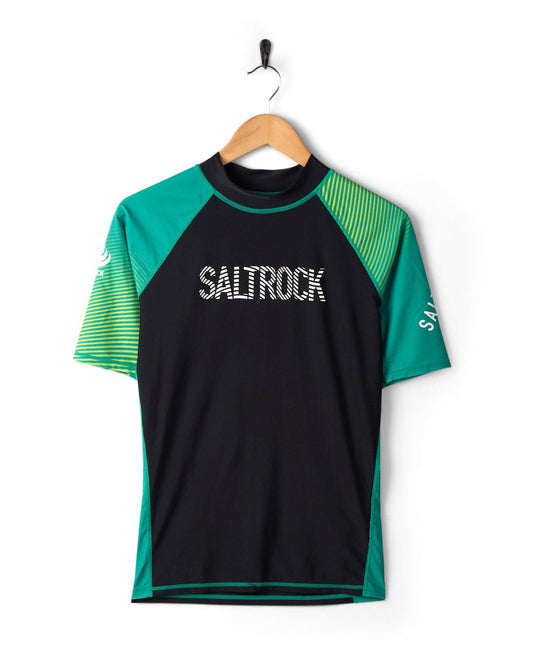 A black and green DNA Wave - Recycled Mens Short Sleeve Rashvest with the word "saltrock" printed in white, featuring UPF 50 protection, hanging on a white wall.