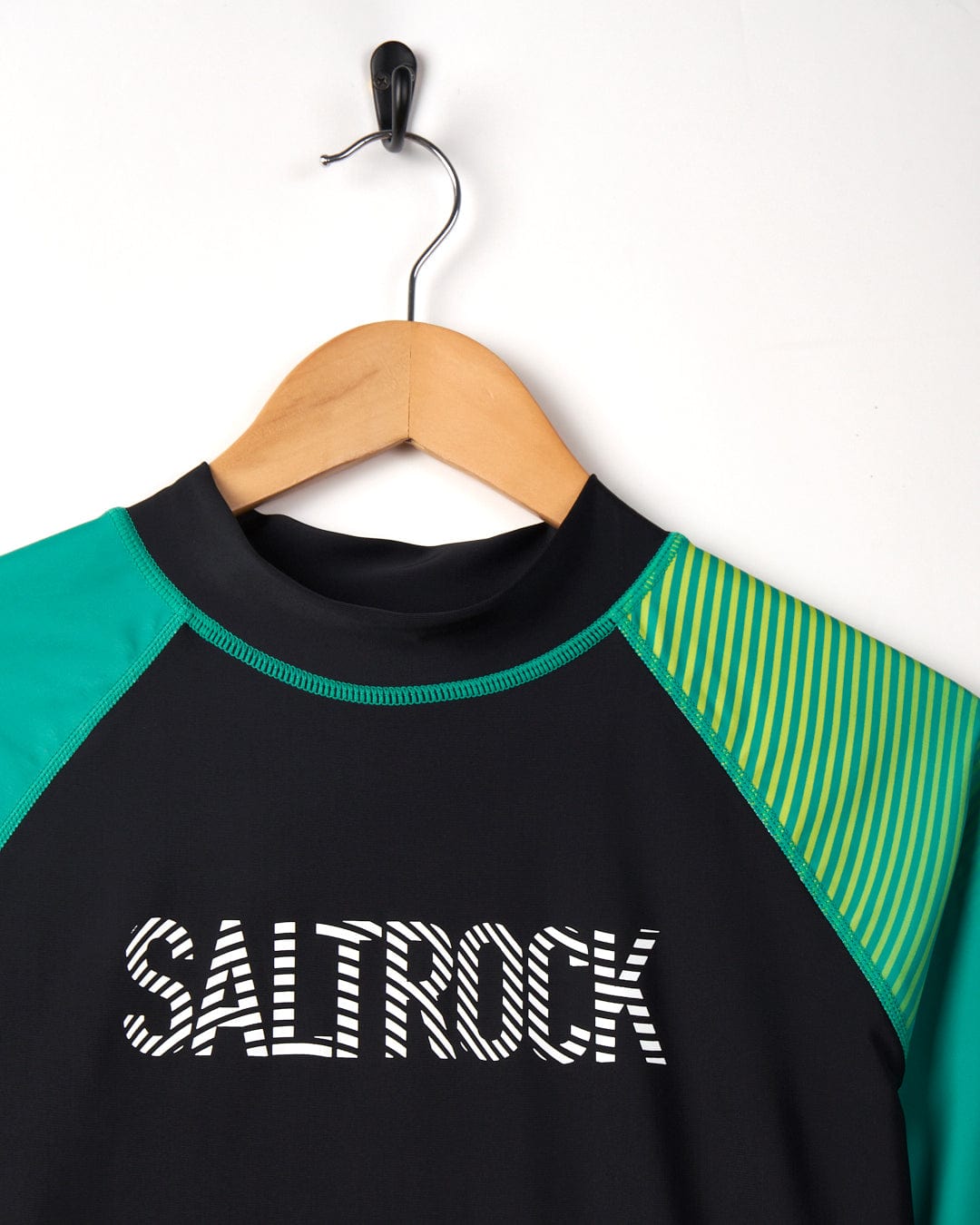 A black and green Saltrock DNA Wave - Recycled Mens Short Sleeve Rashvest hung on a wooden hanger against a white background.