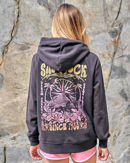 A woman wearing a Saltrock Dreamseeker Gradient - Womens Pop Hoodie - Dark Grey, a dark grey hoodie with a cosy and bold illustration, standing next to rocks.