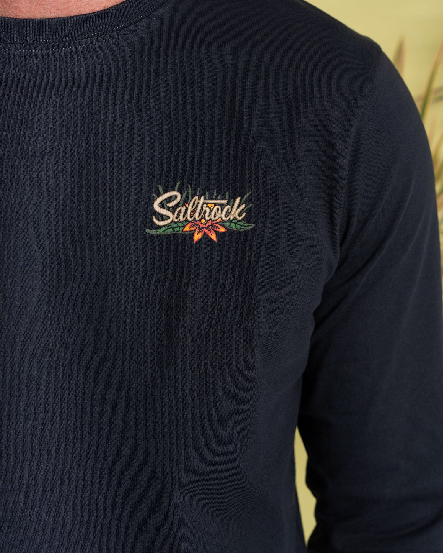 A person wearing a dark grey men's long sleeve t-shirt made by Saltrock, featuring a small, stylish logo on the chest.