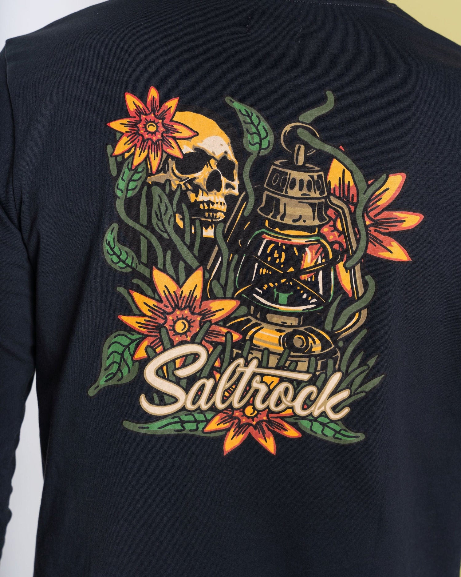 The Lantern Men's Long Sleeve T-shirt by Saltrock in dark grey boasts vibrant graphics of a skull, flowers, and a lantern with "Saltrock" text. Made from 100% cotton, it merges comfort and style perfect for casual outings.