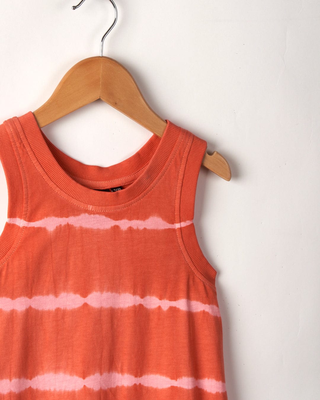 An Eliana - Kids Tie Dye Vest Dress - Peach featuring Saltrock branding hangs on a wooden hanger against a beige background.