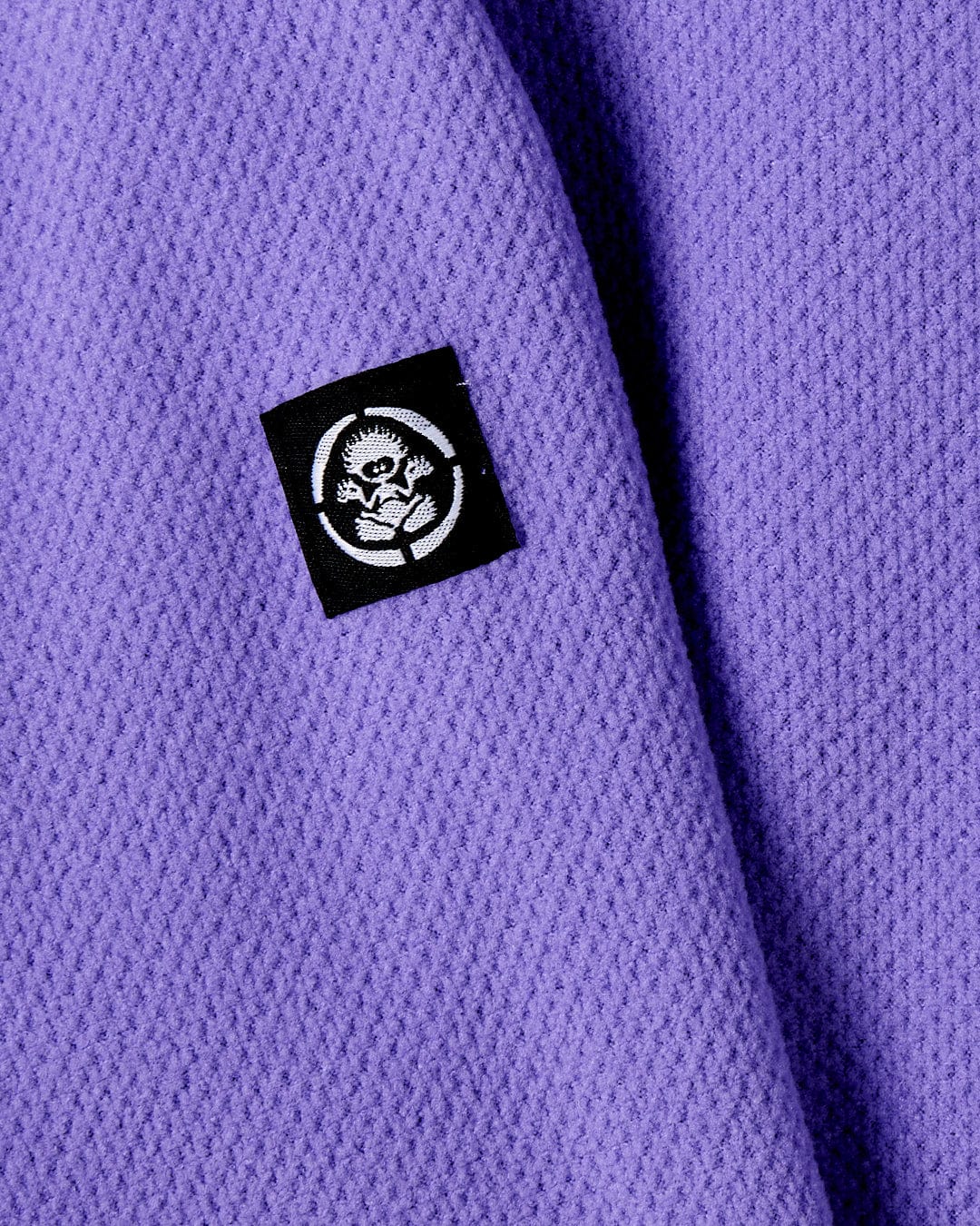 A close up of a Saltrock Ella - Girls 1/4 Neck Fleece in purple with a skull logo on it made from recycled material.