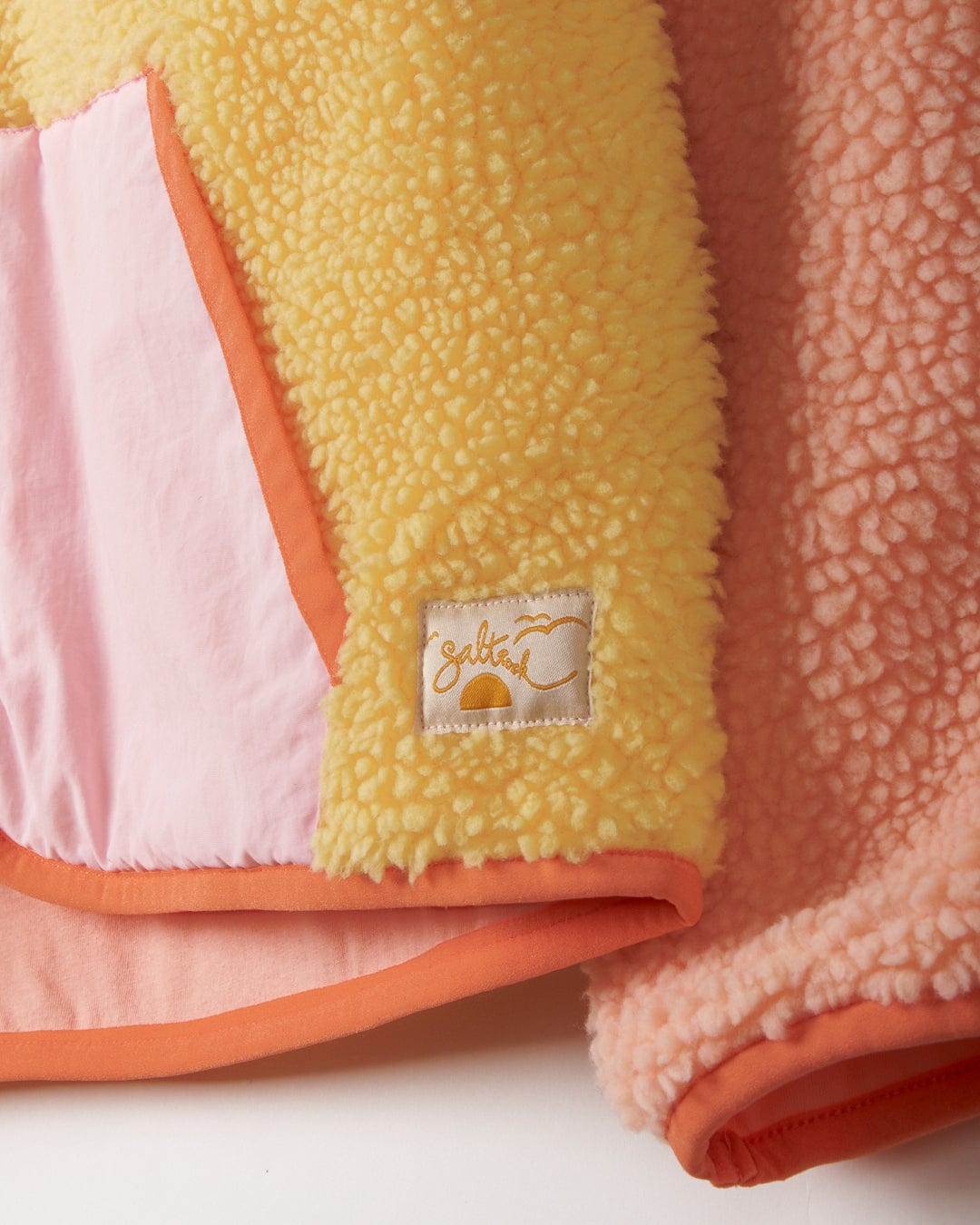 A yellow and pink Saltrock Sherpa fleece blanket with a yellow label.