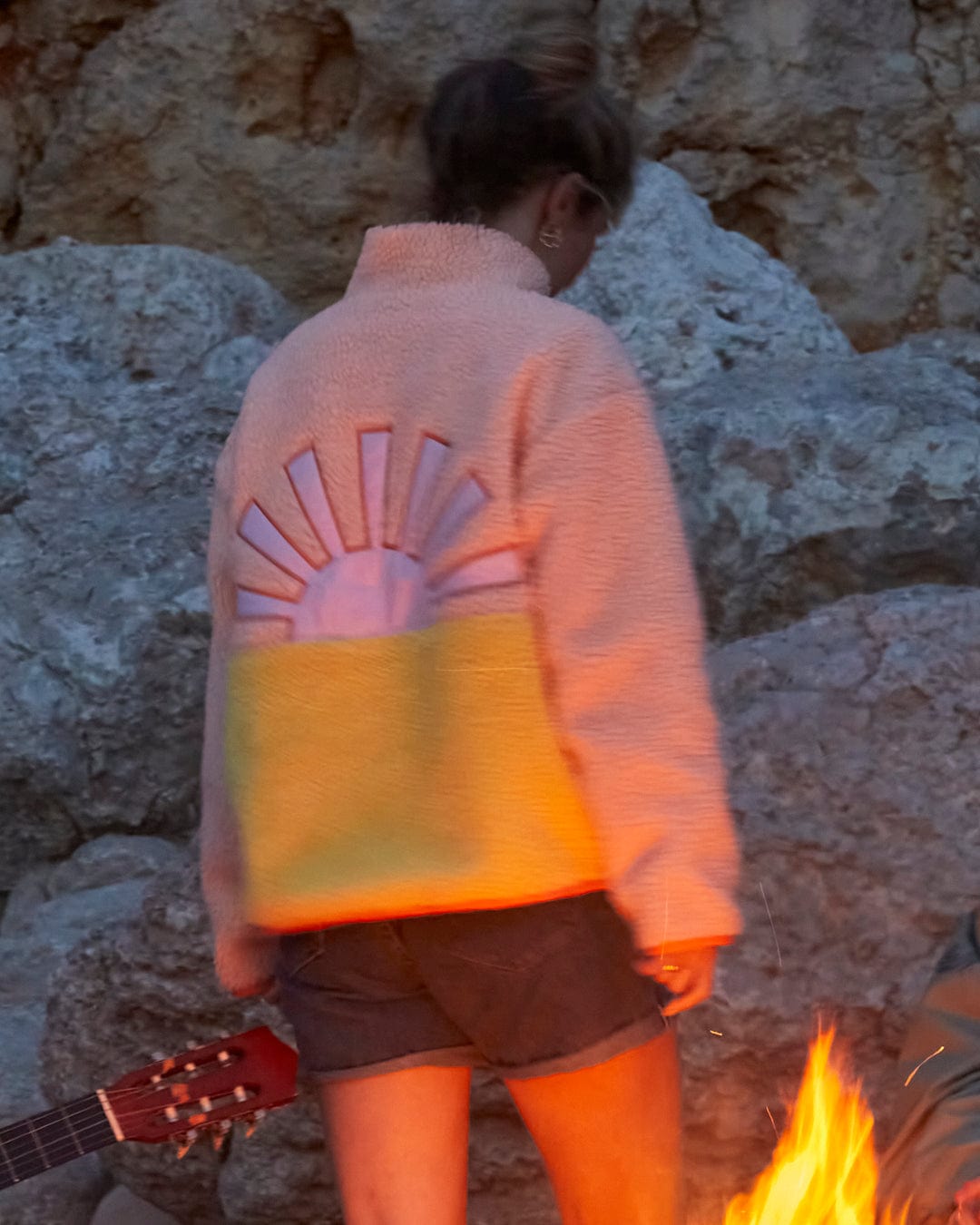 A woman is standing next to a fire with a Emery Sunshine - Womens Sherpa Fleece - Coral by Saltrock.