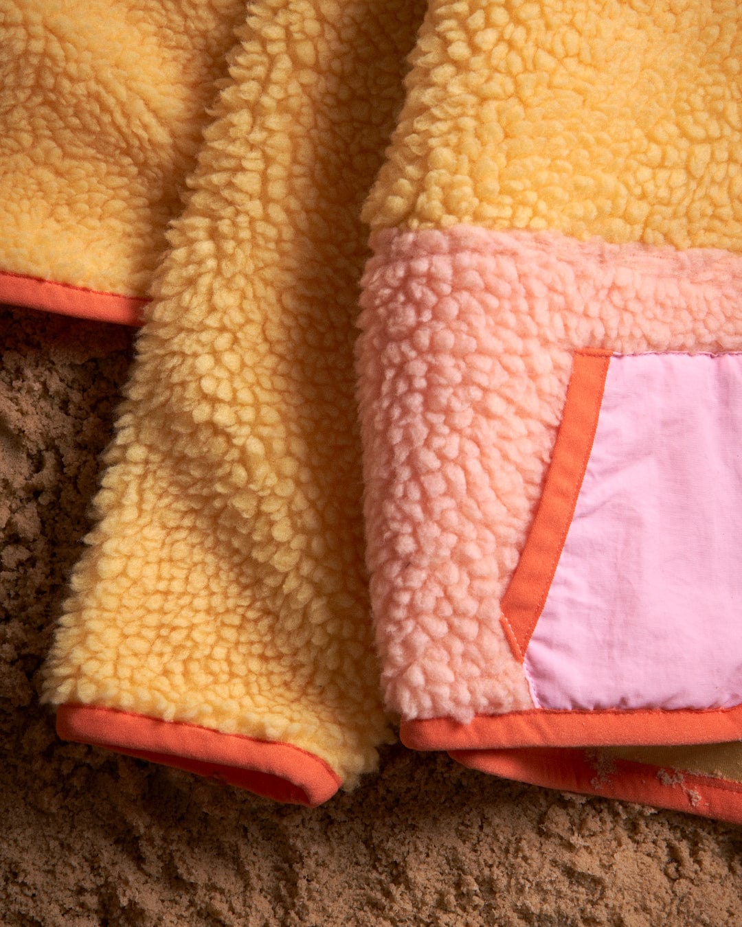 A yellow and pink Emery Sunshine - Kids Sherpa Fleece jacket by Saltrock is laying on the ground.