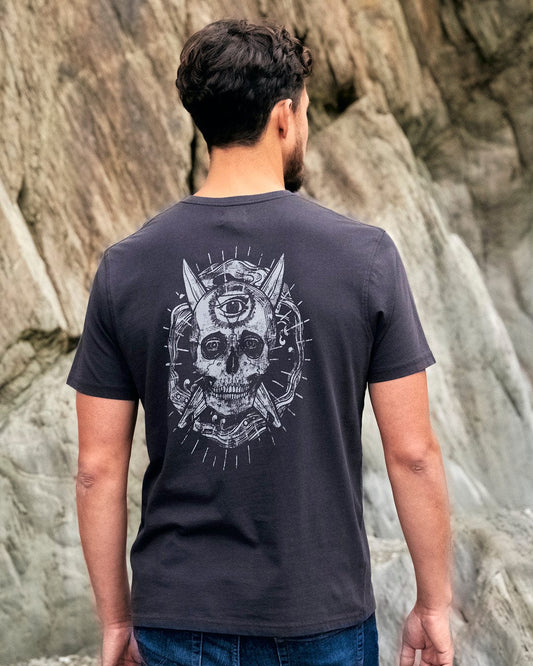 A man wearing a black t-shirt with Saltrock branding featuring a skull design, specifically the Eye Sea Waves - Mens Short Sleeve Stonewash T-shirt in Dark Grey.