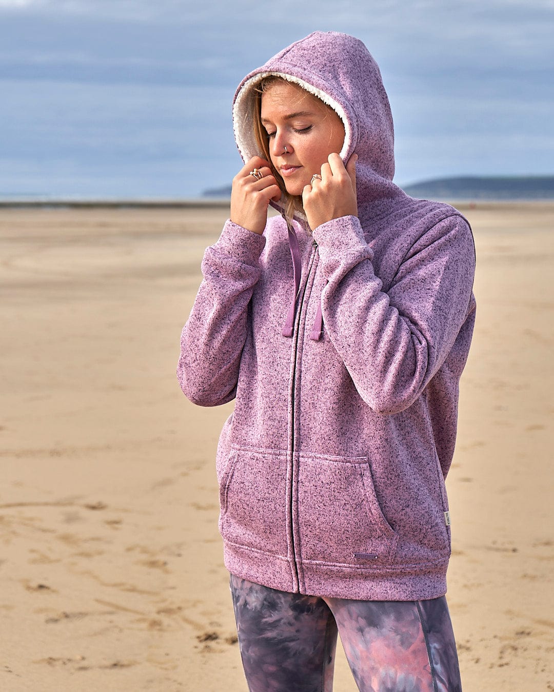 A woman in a Saltrock Farley - Lined Zip Hoodie - Purple standing on the beach.