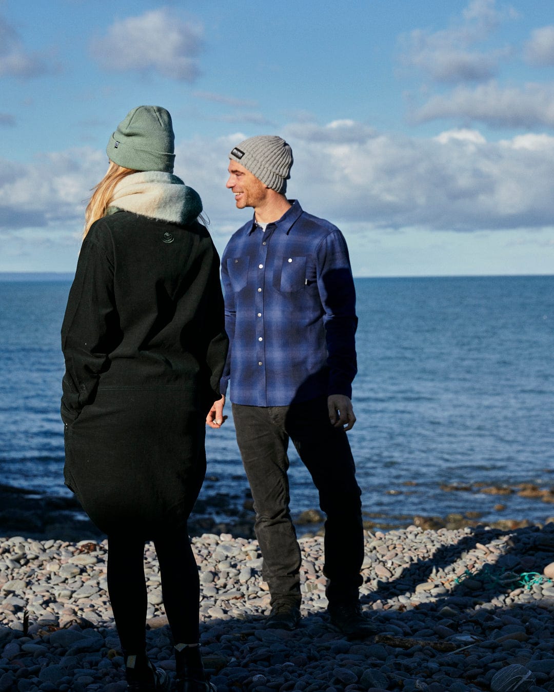A man and woman standing on a rocky beach looking at the ocean, wearing Farris - Mens Check Shirts in Blue, branded by Saltrock.