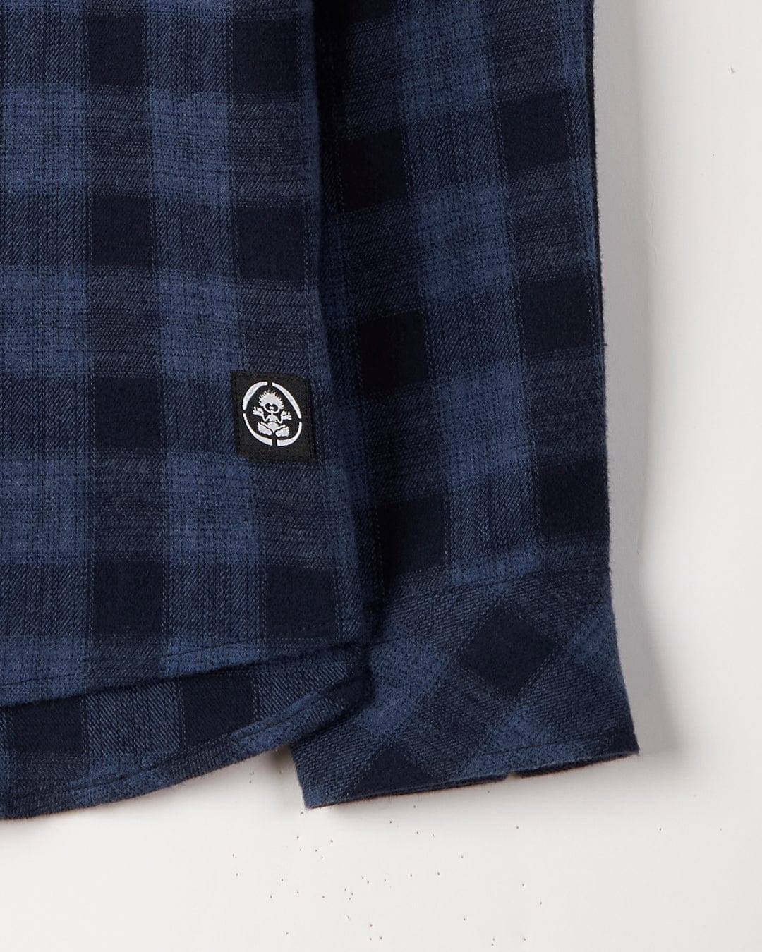 Close-up of a navy blue and black check print garment with a Saltrock branded tag, made of 100% Cotton.