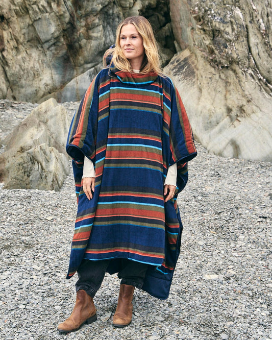 A woman wearing a Saltrock Festival Reversible Poncho - Blue standing on a rock.