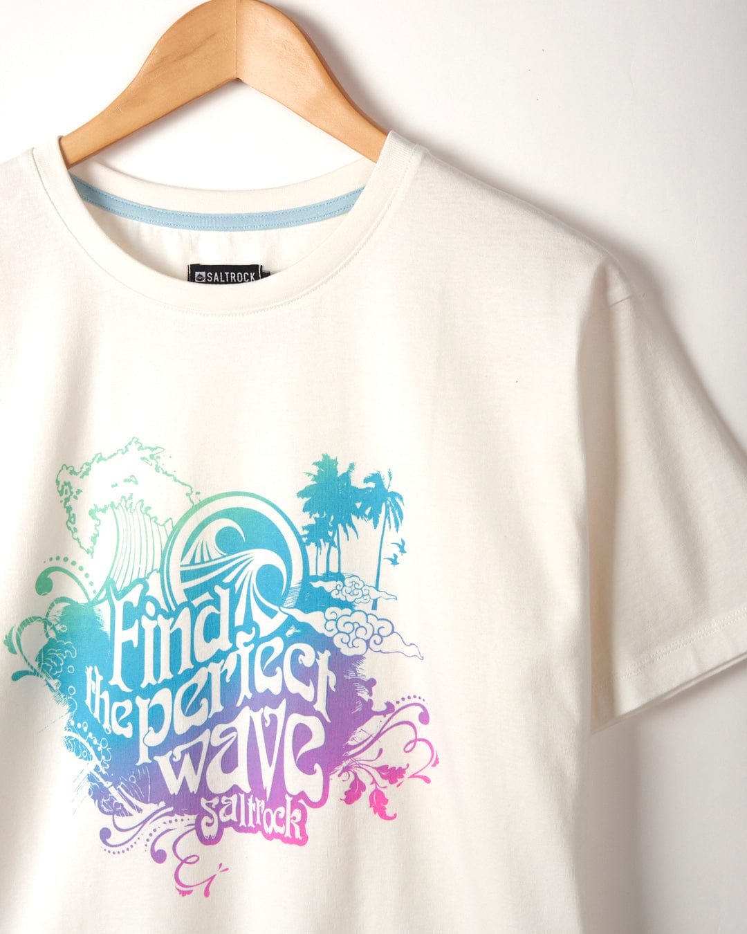 White "Find The Perfect Wave" Womens Short Sleeve T-Shirt by Saltrock hanging on a wooden hanger against a plain background.