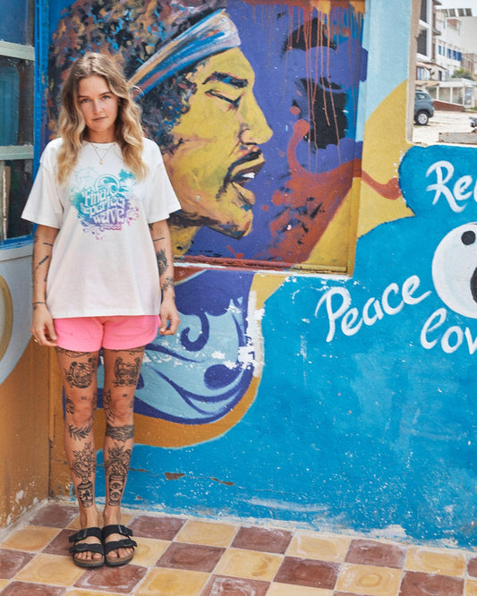 Woman with tattoos standing next to a multi-coloured mural featuring a portrait and peace symbols wearing the Find The Perfect Wave - Womens Short Sleeve T-Shirt by Saltrock.