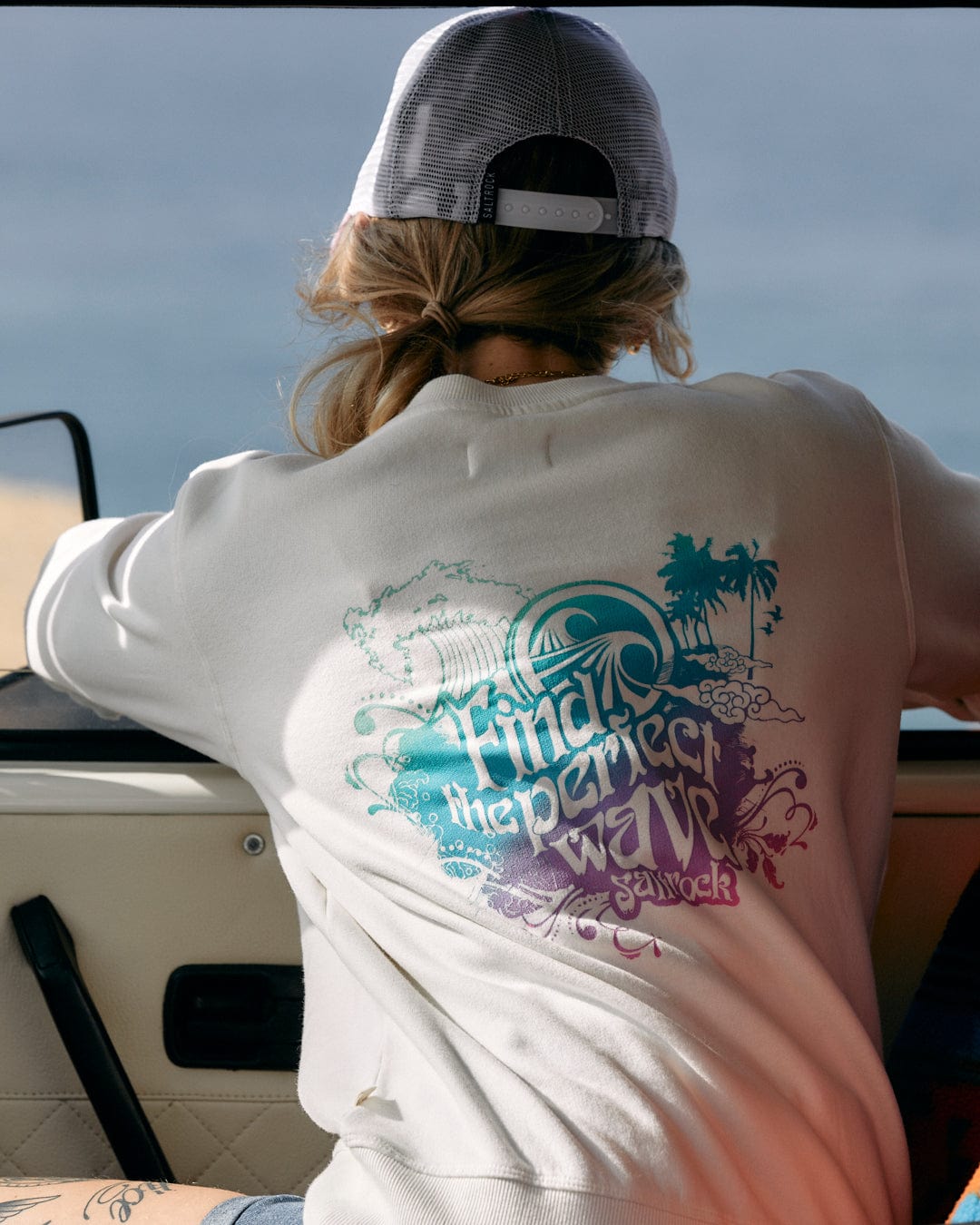 A woman sitting in a car looking at the Saltrock Find The Perfect Wave - Womens Sweat - White.