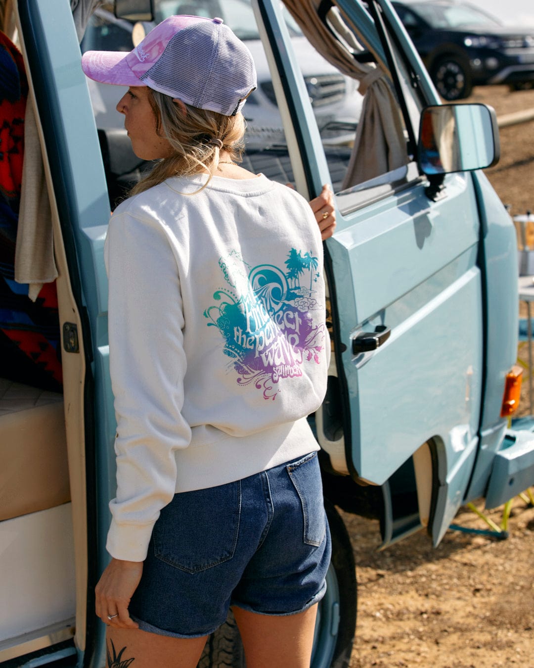 Woman standing by a van wearing a Saltrock crew neck t-shirt with a multi-coloured slogan and denim shorts.