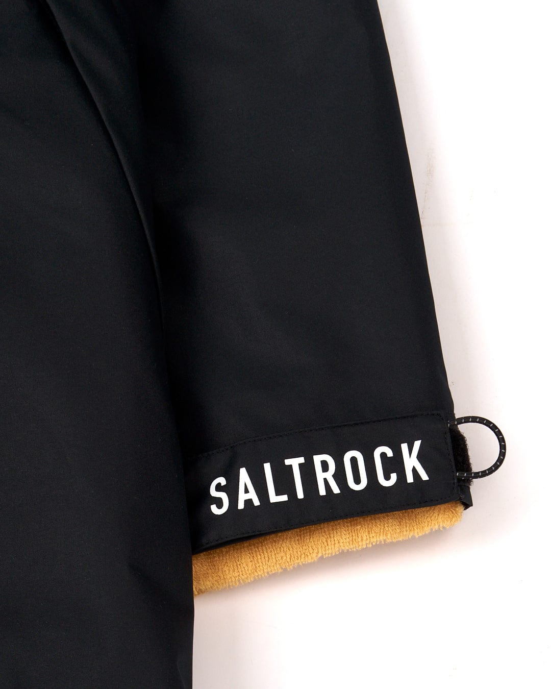Close-up view of a Saltrock black jacket with a "3 in 1 Recycled Four Seasons Changing Robe - Black/Yellow" brand tag on the cuff over a tan towelling lining.