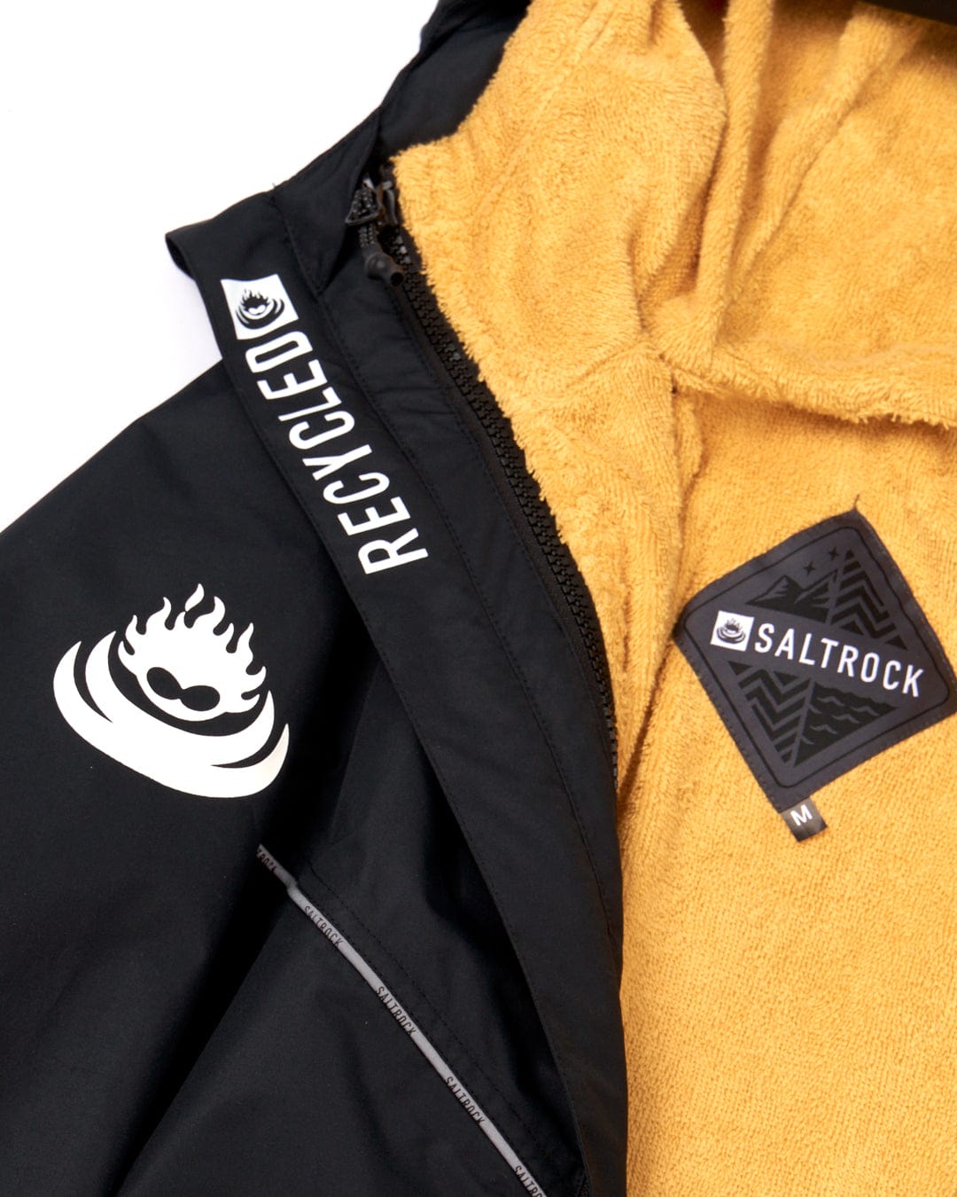 Close-up of a Saltrock black jacket with white "recycled material" text and logo next to a Saltrock yellow fleece garment with a "Saltrock" brand patch.