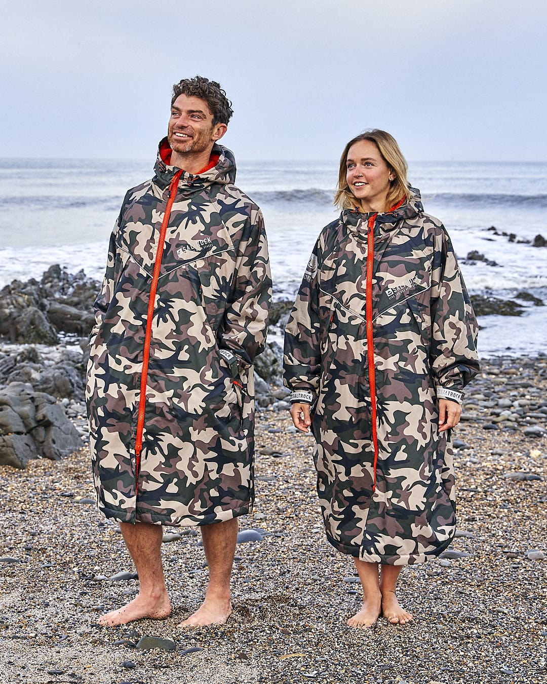 Two people standing on a beach wearing Saltrock's Four Seasons - Waterproof Changing Robe in Brown.