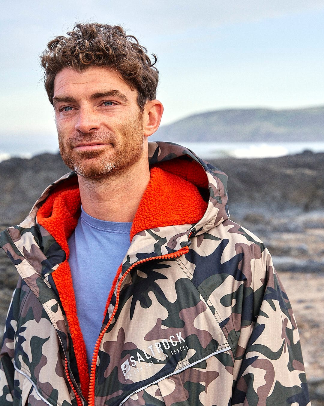 A man in a Saltrock camouflage jacket standing on the beach.