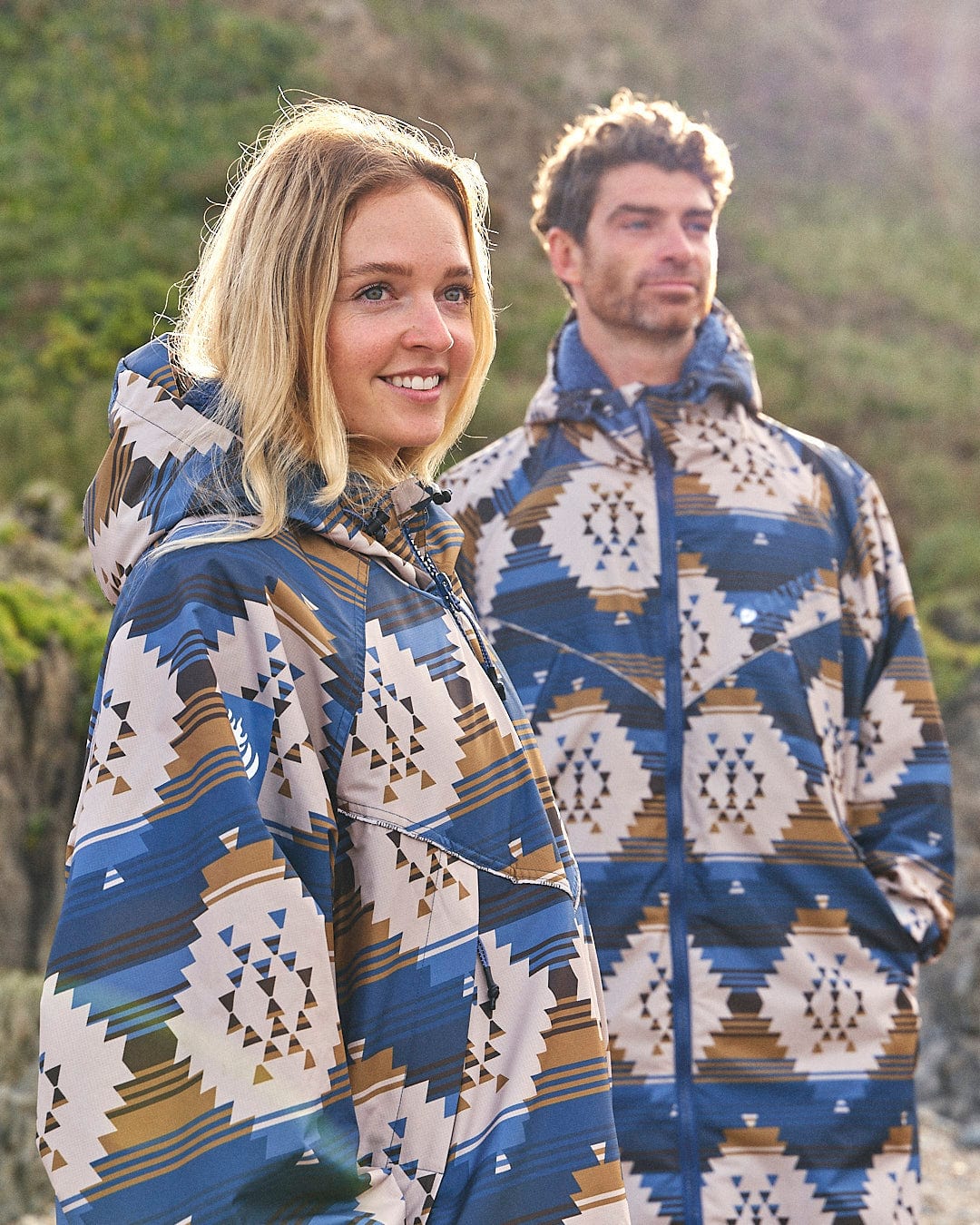 A man and woman standing next to each other in a Saltrock Four Seasons Changing Robe - Aztec poncho.