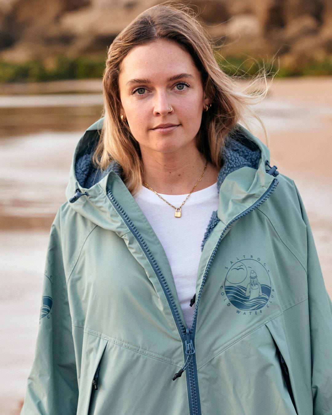 Woman in an oversized Saltrock Recycled Four Seasons Changing Robe - Light Green standing on a beach at dusk.