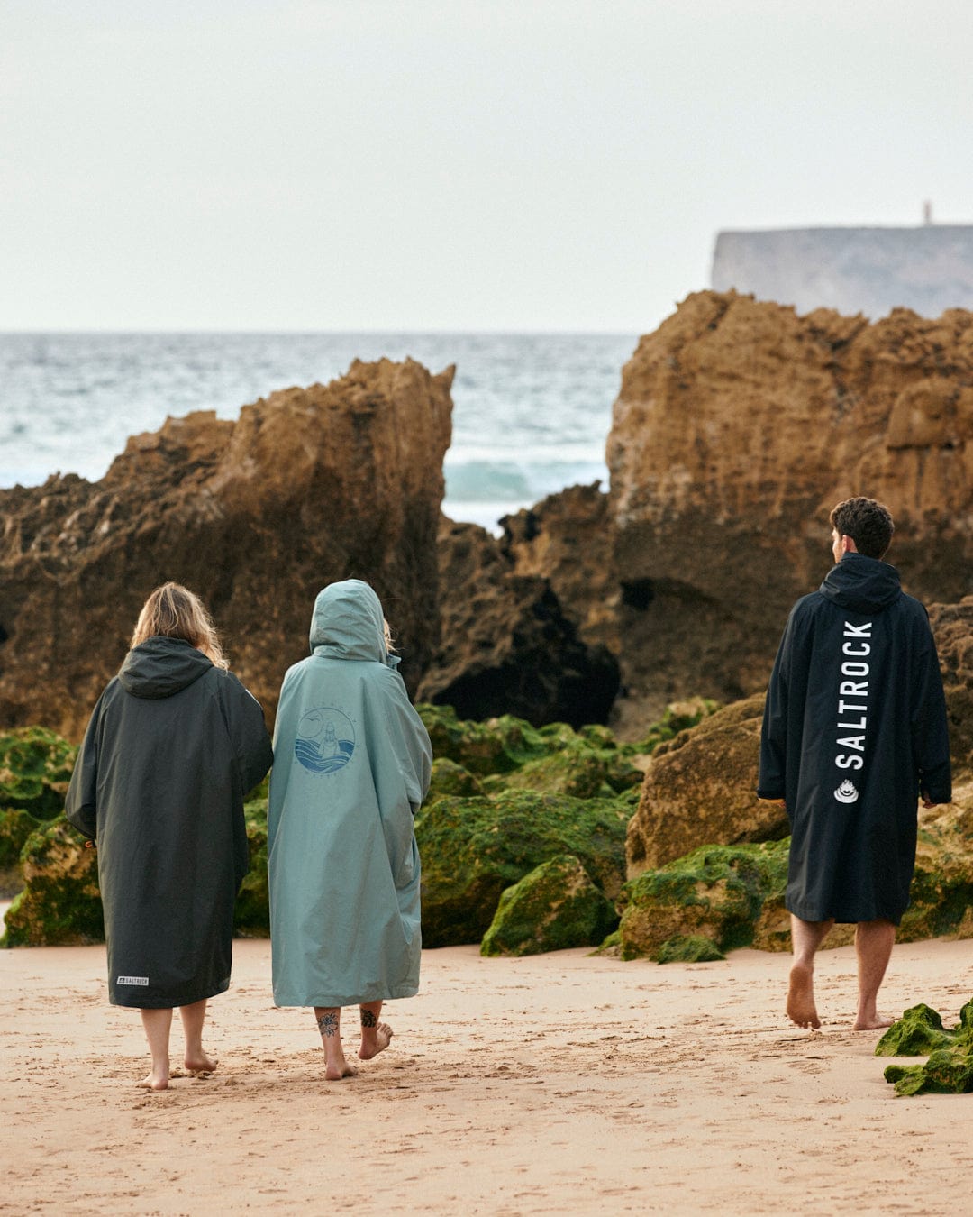 Three individuals in Saltrock Recycled Four Seasons Changing Robbe - Green/Aztec with fleece lining walking on the beach.