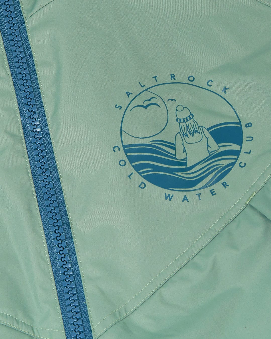 Close-up of a light green, waterproof Recycled Four Seasons Changing Robe with a Saltrock logo and a blue zipper detail.