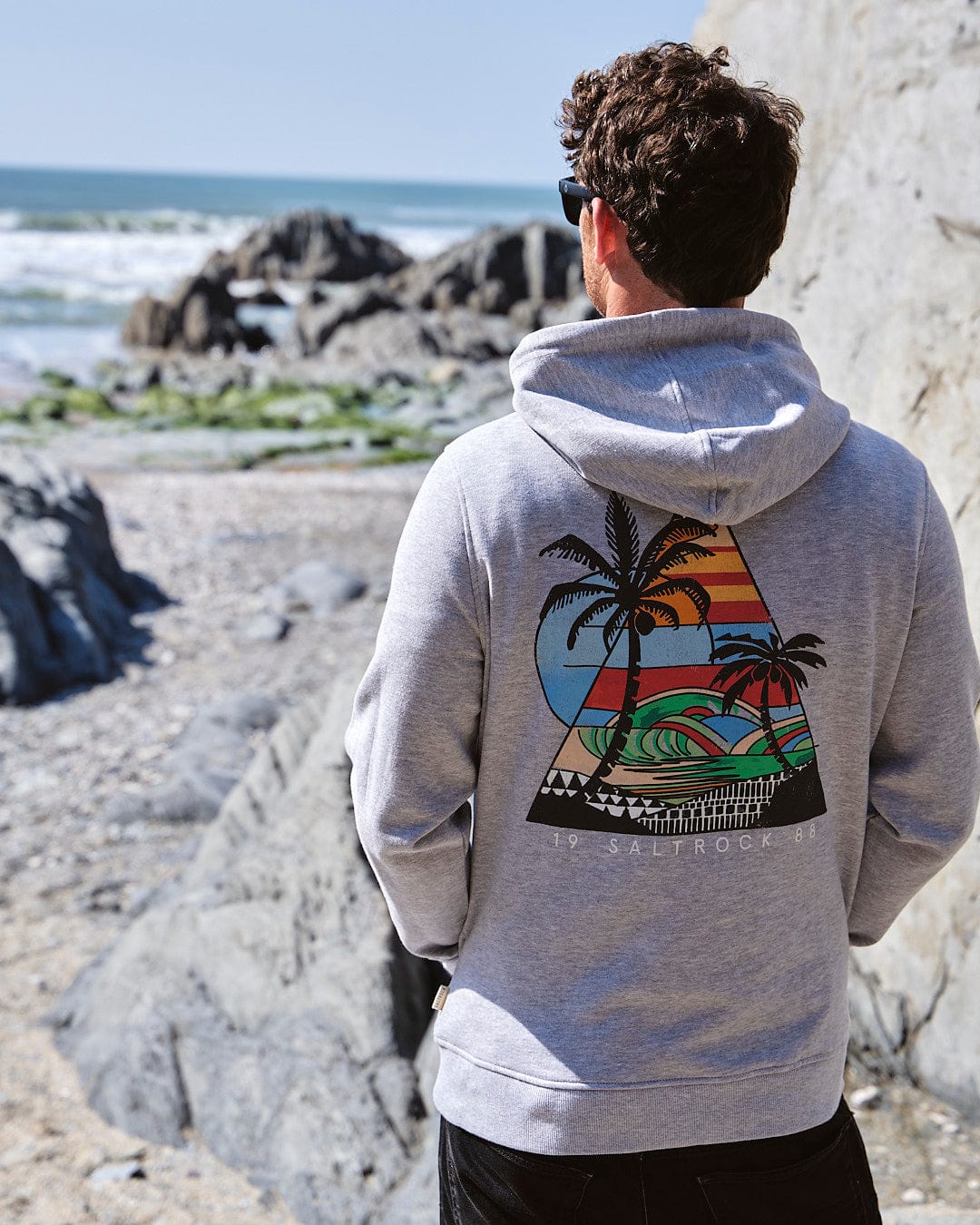 The back of a man wearing a Saltrock Geo Beach - Mens Pop Hoodie - Grey with a palm tree on it.