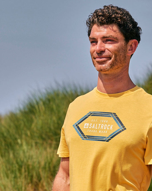 A man wearing a Saltrock Gradient Hex - Mens Short Sleeve T-Shirt - Yellow standing in a field.