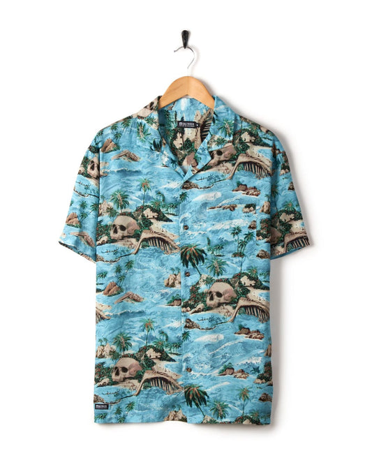 A colorful Hawaiian Isle short sleeve shirt in blue with tropical and skull island print patterns, displayed on a wooden hanger against a white background. Brand name: Saltrock.