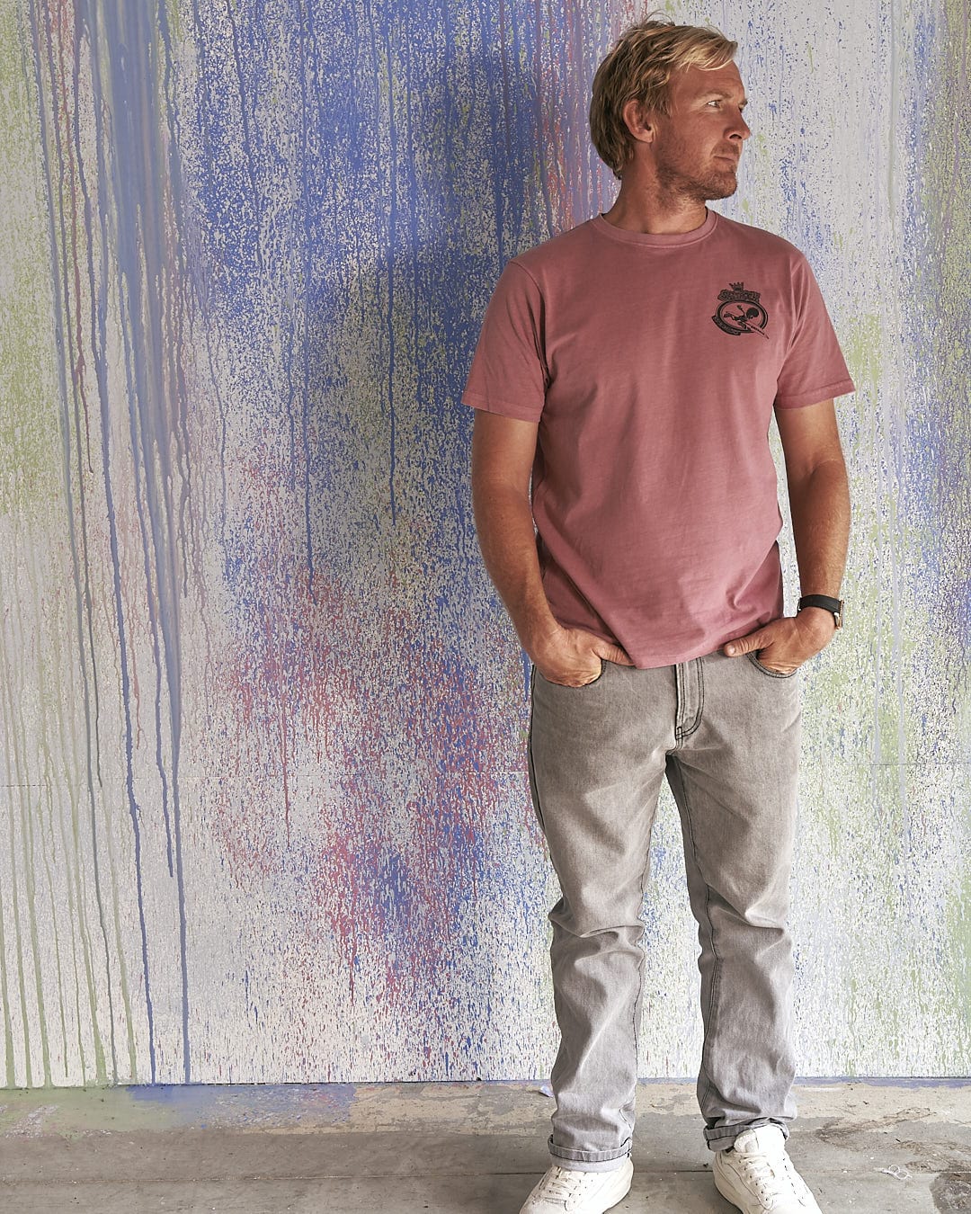A man in a Heraldic Tok - Limited Edition 35 Years T-Shirt by Saltrock standing in front of a colorful wall.