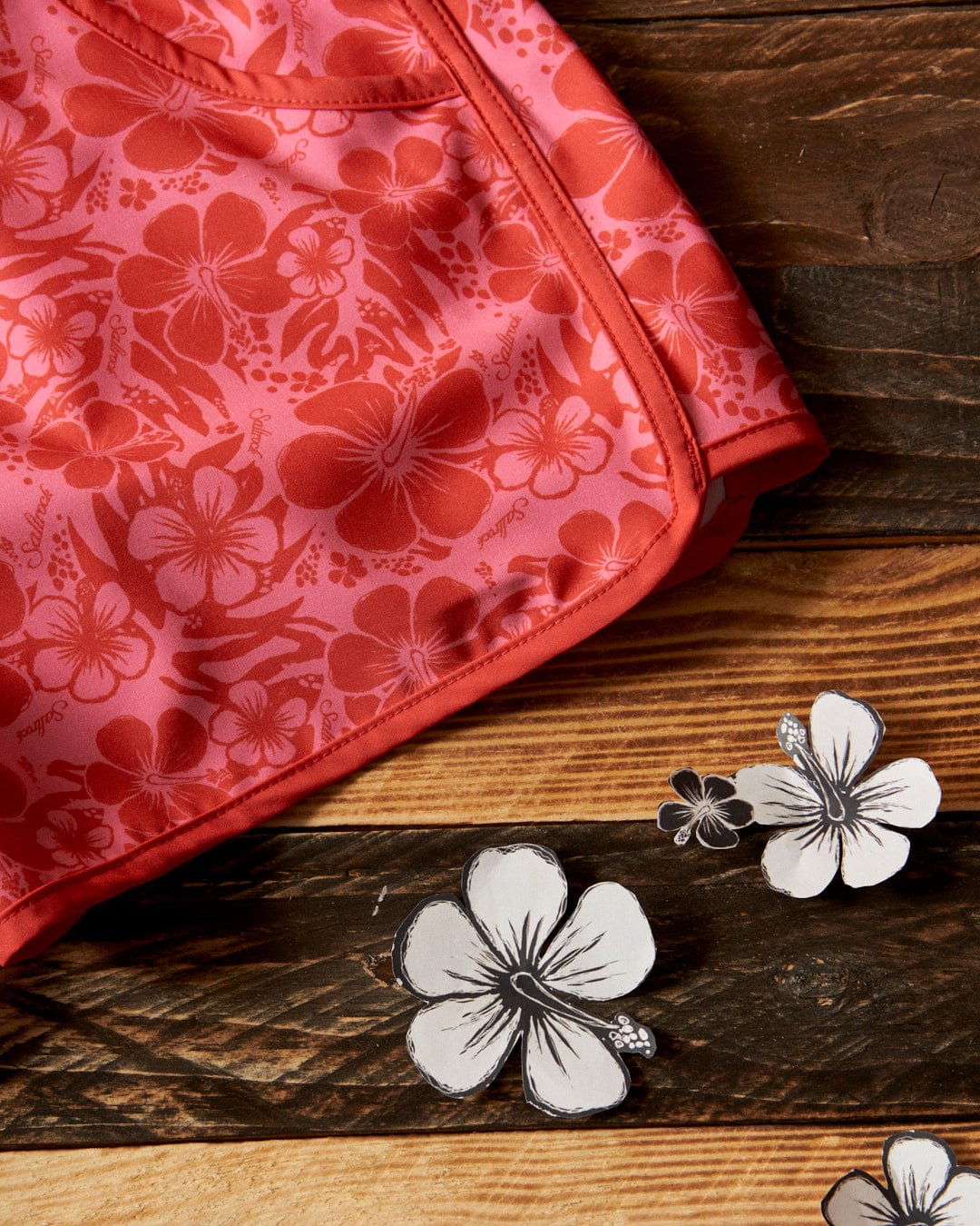 Saltrock's Hibiscus - Womens Boardshorts - Red/Pink with floral print on a wooden table.