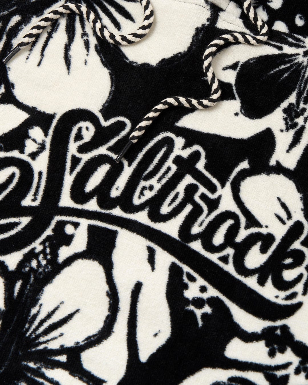 Close-up of a Saltrock Hibiscus Changing Towel in black and white fabric with a floral and text design, featuring the word "Saltrock" in cursive script.